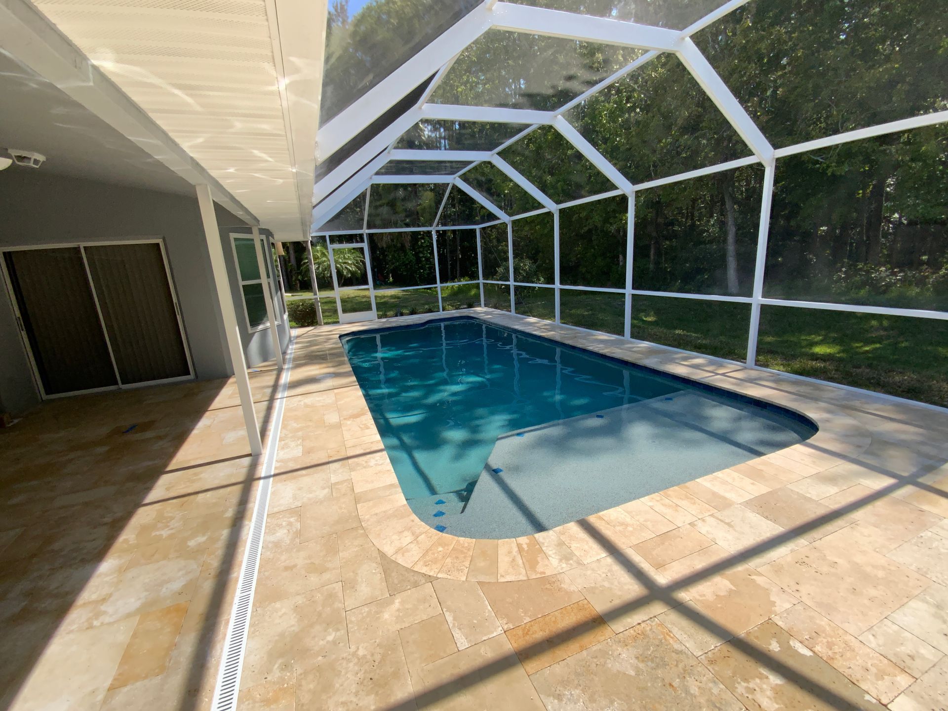 Pool enclosed by white screen, tan tiles surround it. Sliding doors on the left, trees in the background.