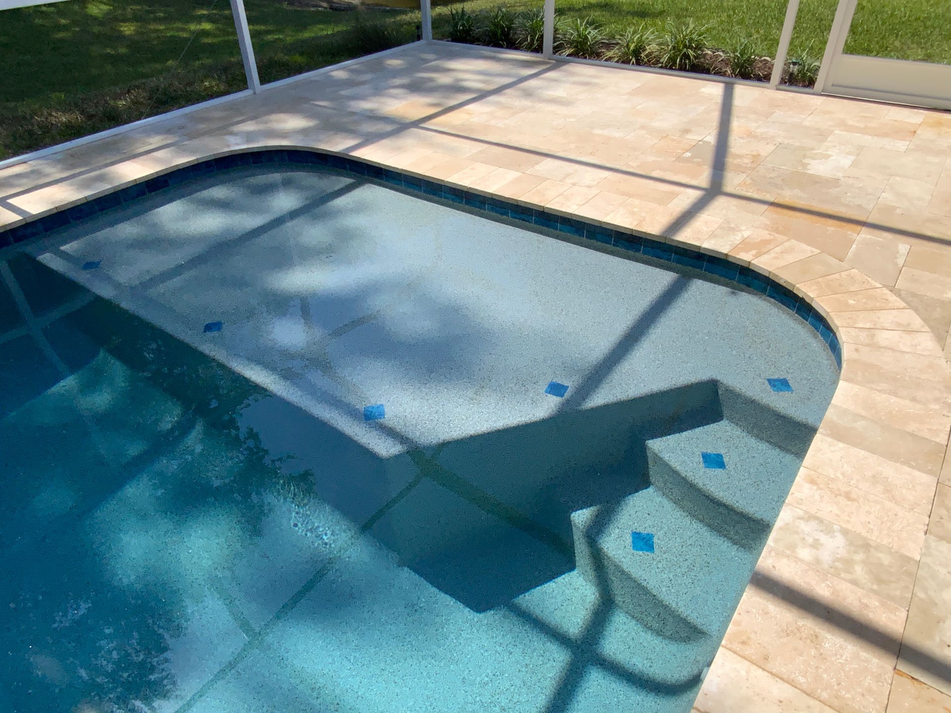 Pool with steps and light blue water, surrounded by tan patio and white screened enclosure.