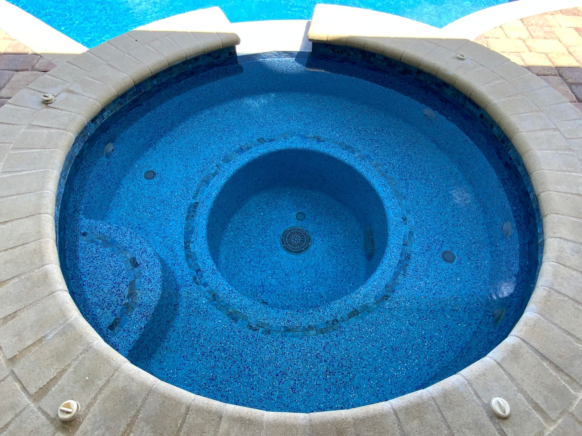 Circular blue hot tub with gray brick surround, viewed from above. Water spills from the top edge.