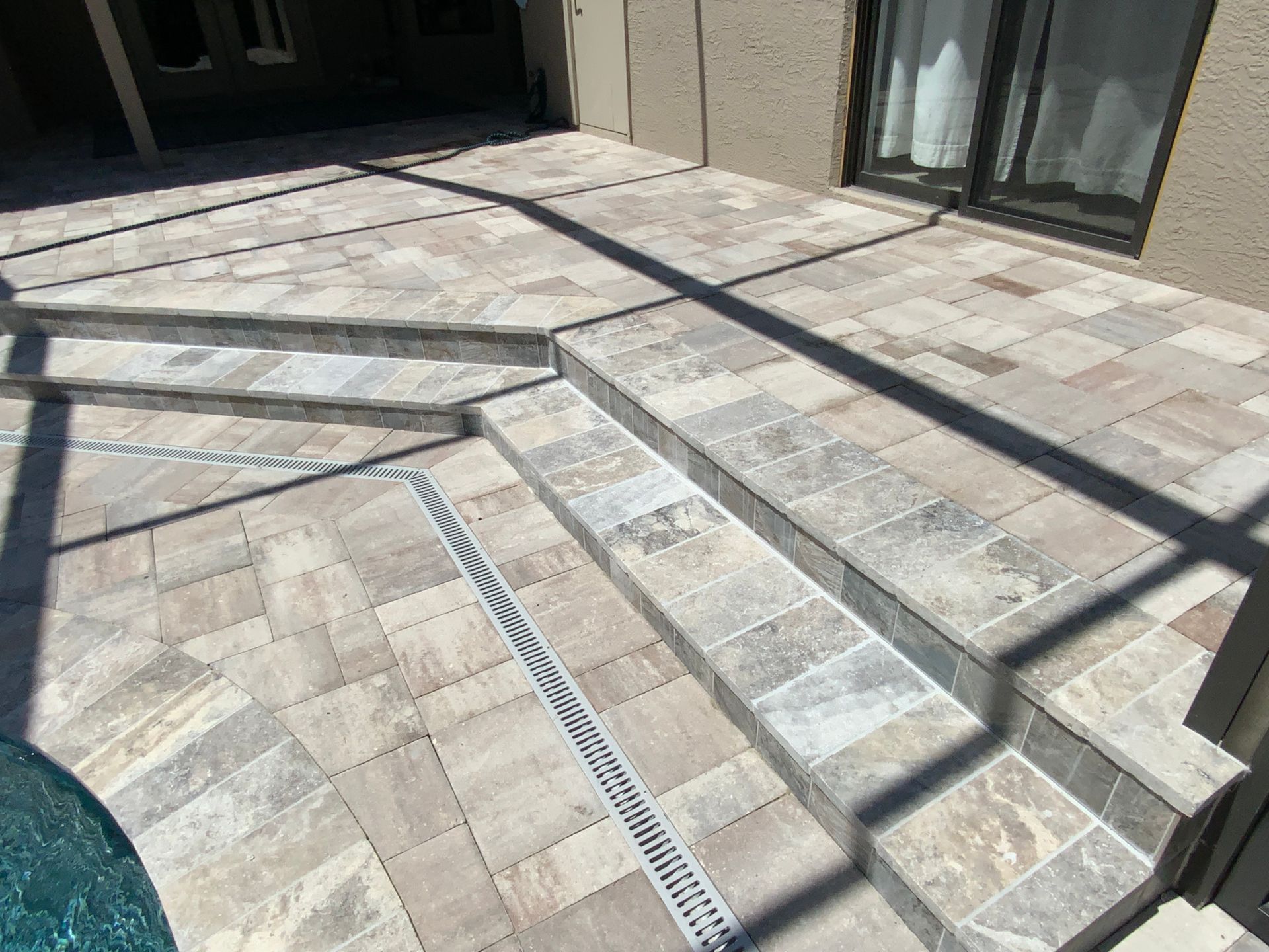 Stone patio with steps leading to a sliding door, next to a pool.