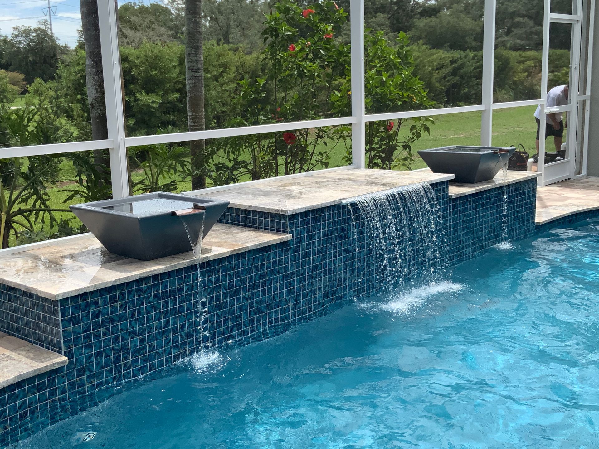 Pool with blue tile waterfall, tan stone ledge, and two dark gray water bowls.