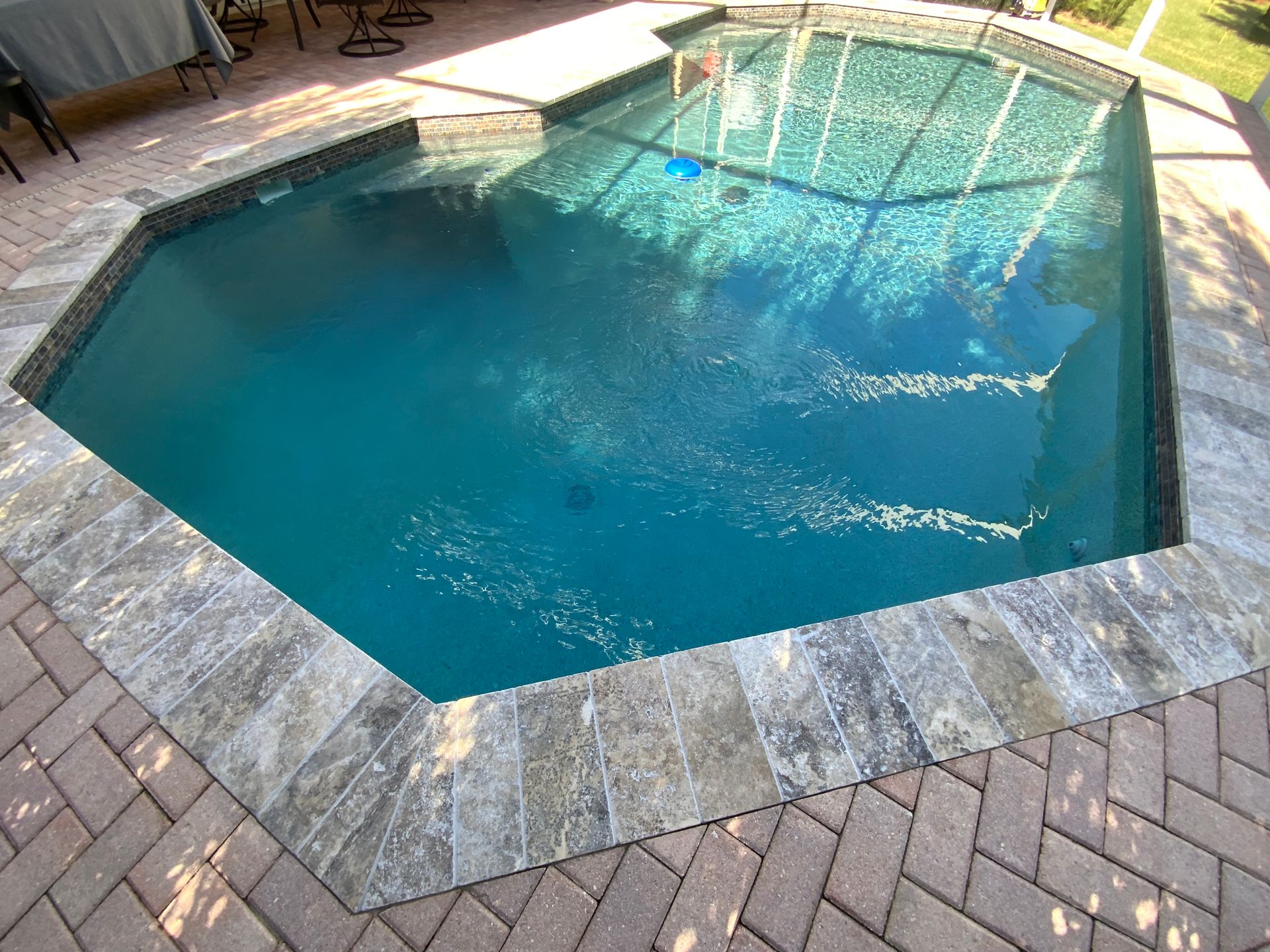 Octagonal swimming pool with blue water, surrounded by gray stone and brick patio.