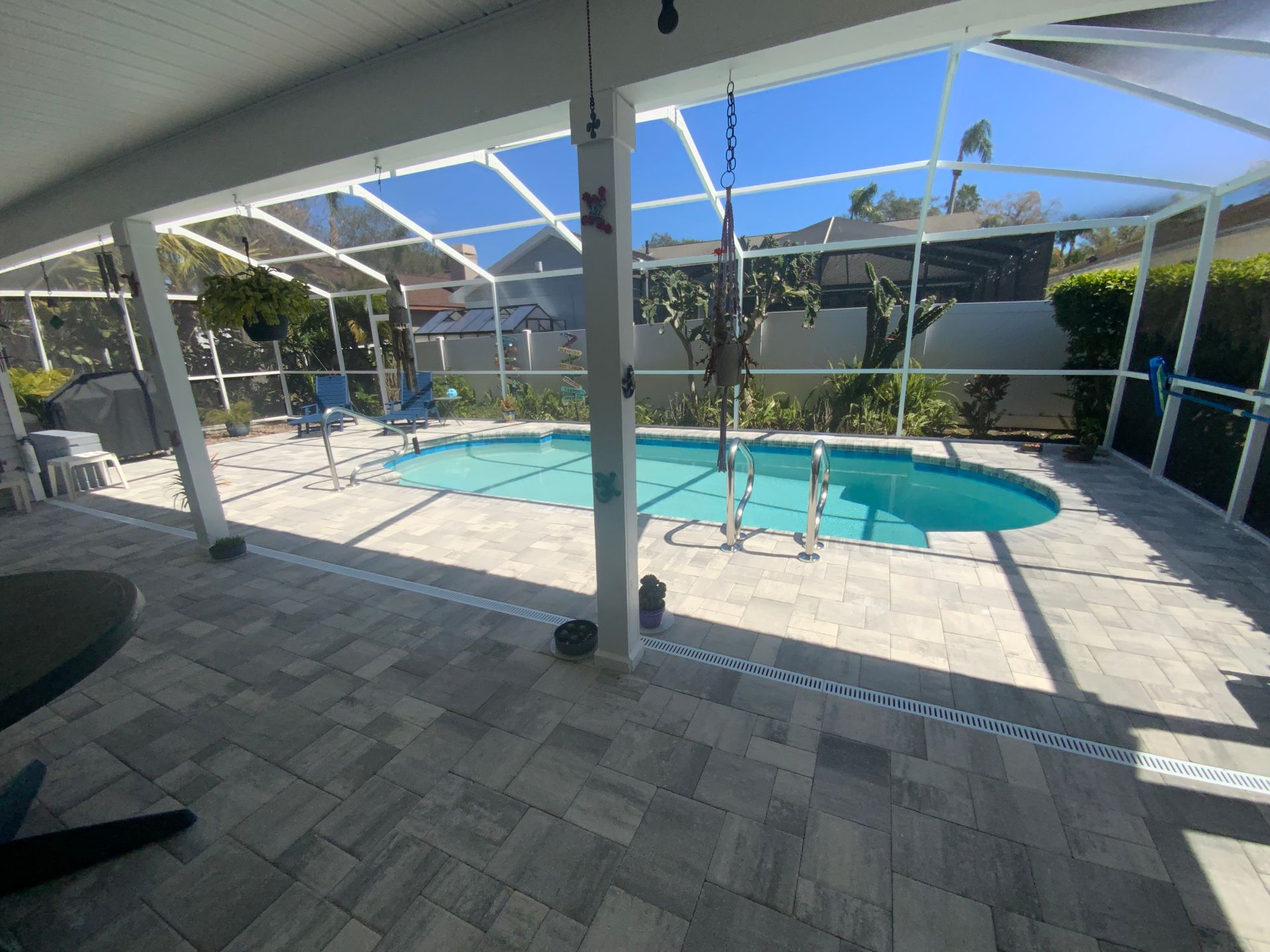 Screened-in patio with pool; gray pavers, blue water, white framing, and clear sky visible through the screen.