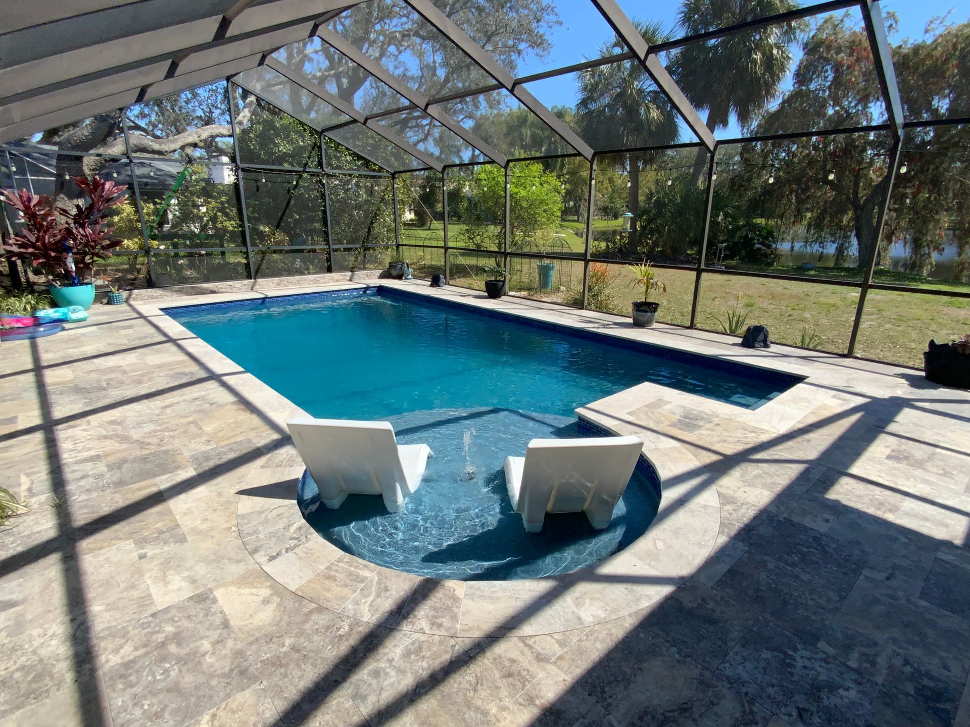 Pool with two white chairs in a screened-in patio, sunny day.