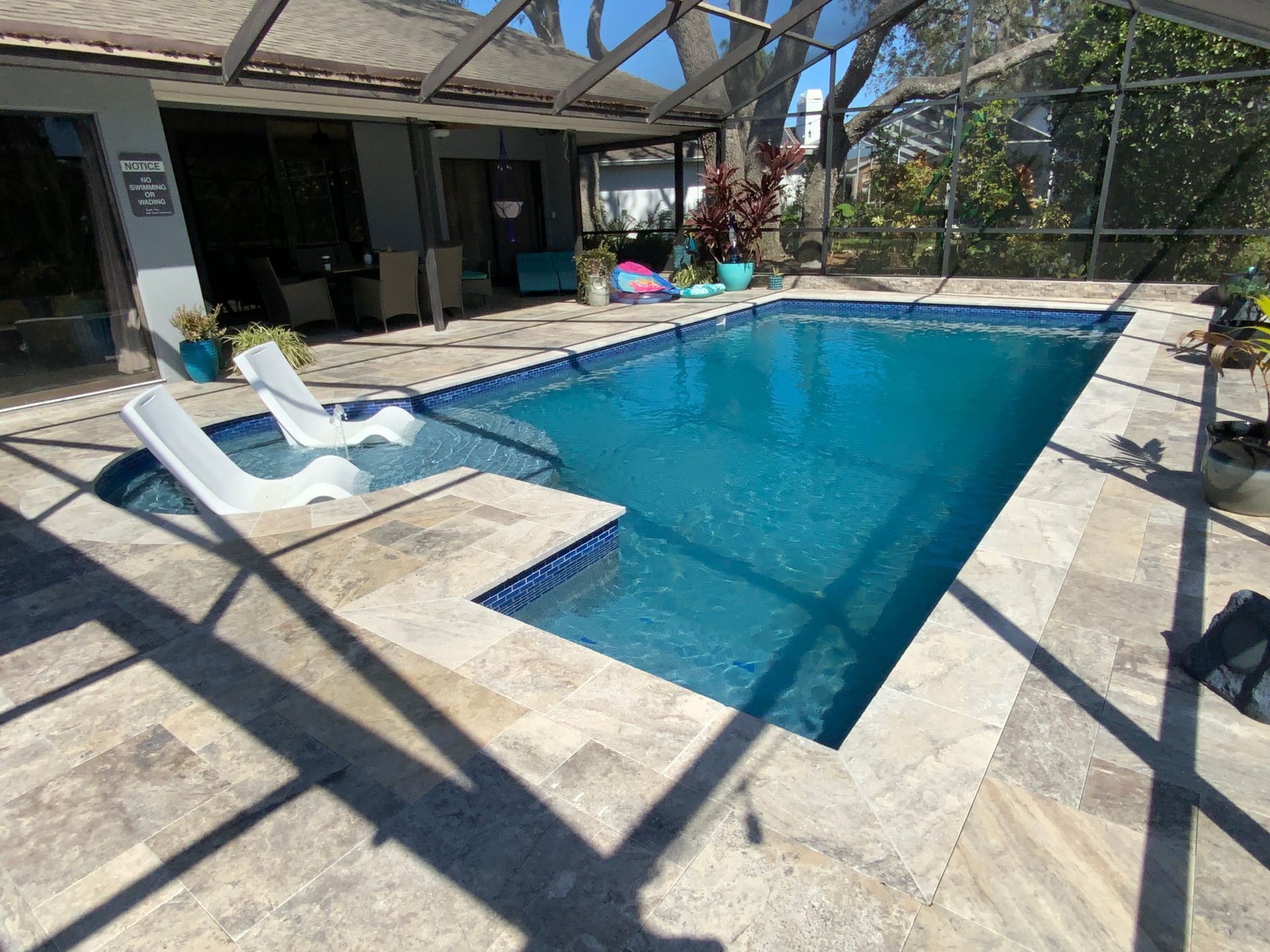 Swimming pool with white lounge chairs, surrounded by stone pavers, screened-in patio in the background.