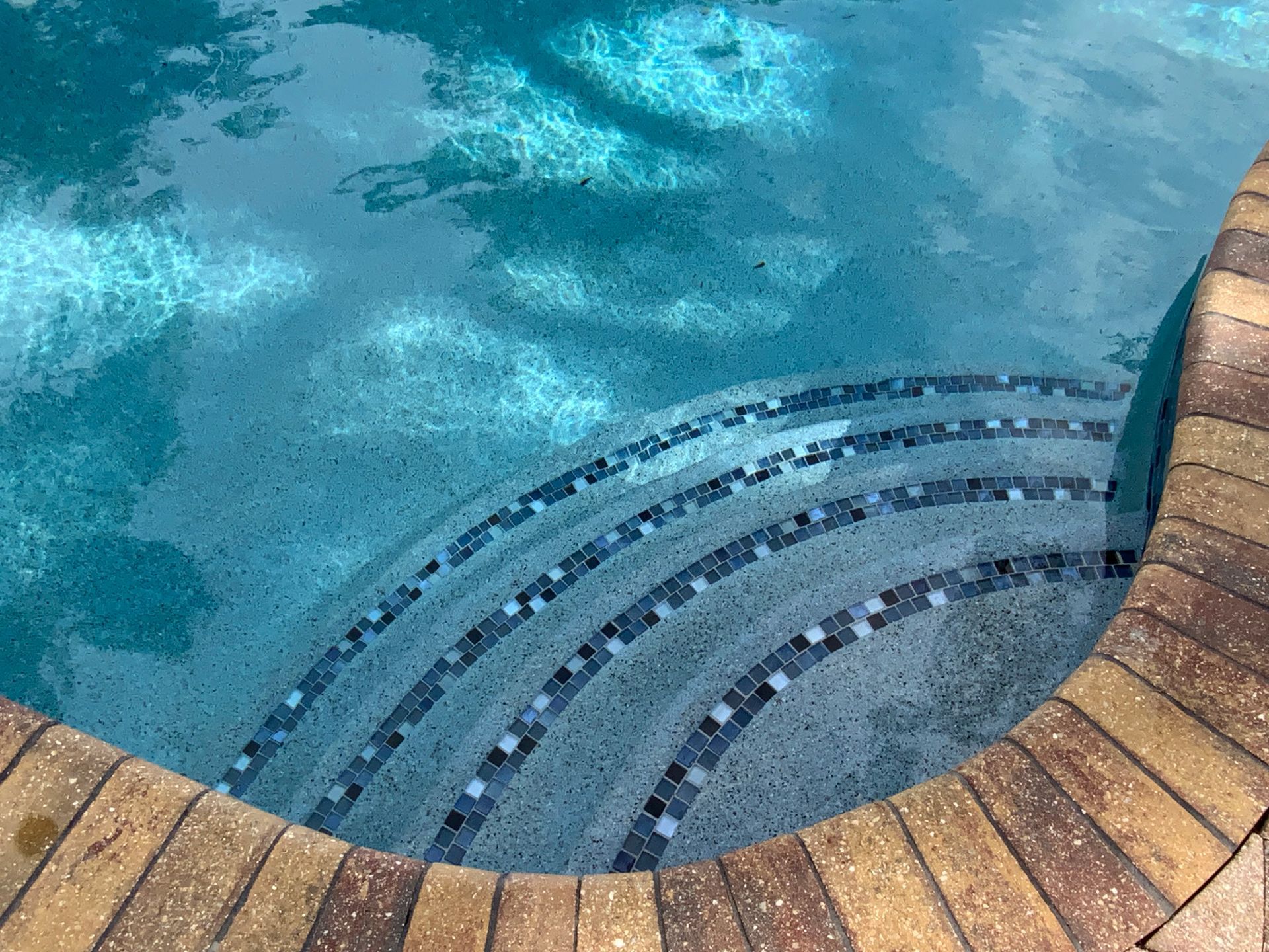 Pool with tiled steps and brick coping. Clear water reflects sunlight.