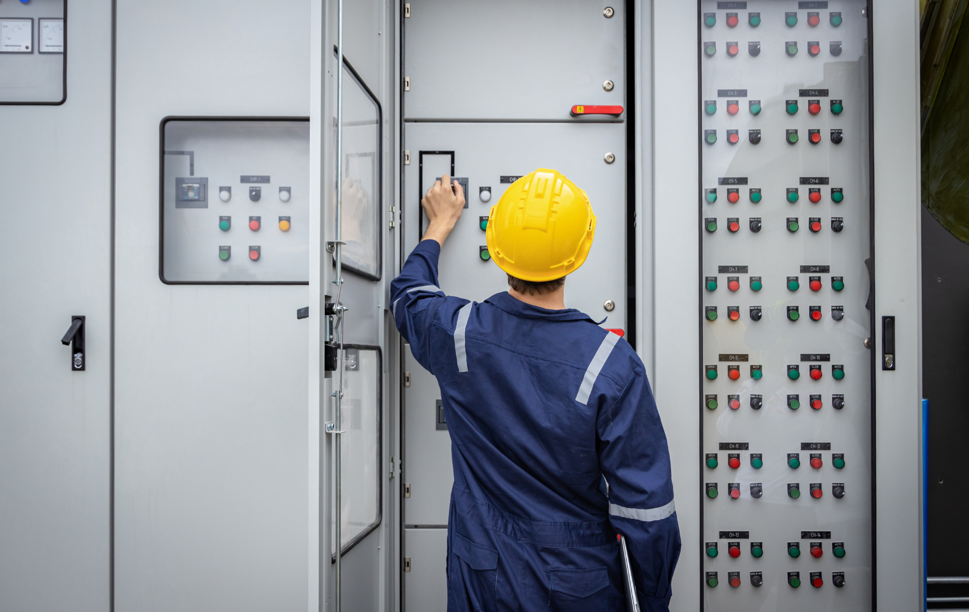 A man in a hard hat is working on a control panel.