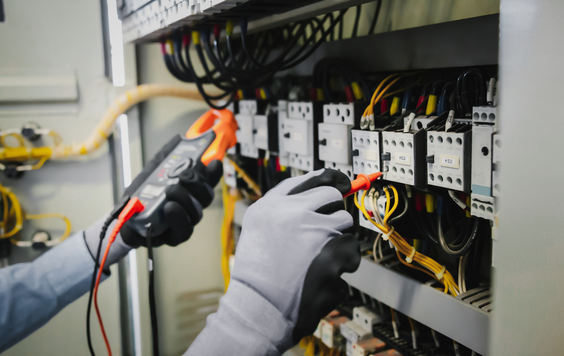 An electrician is working on an electrical panel with a multimeter.
