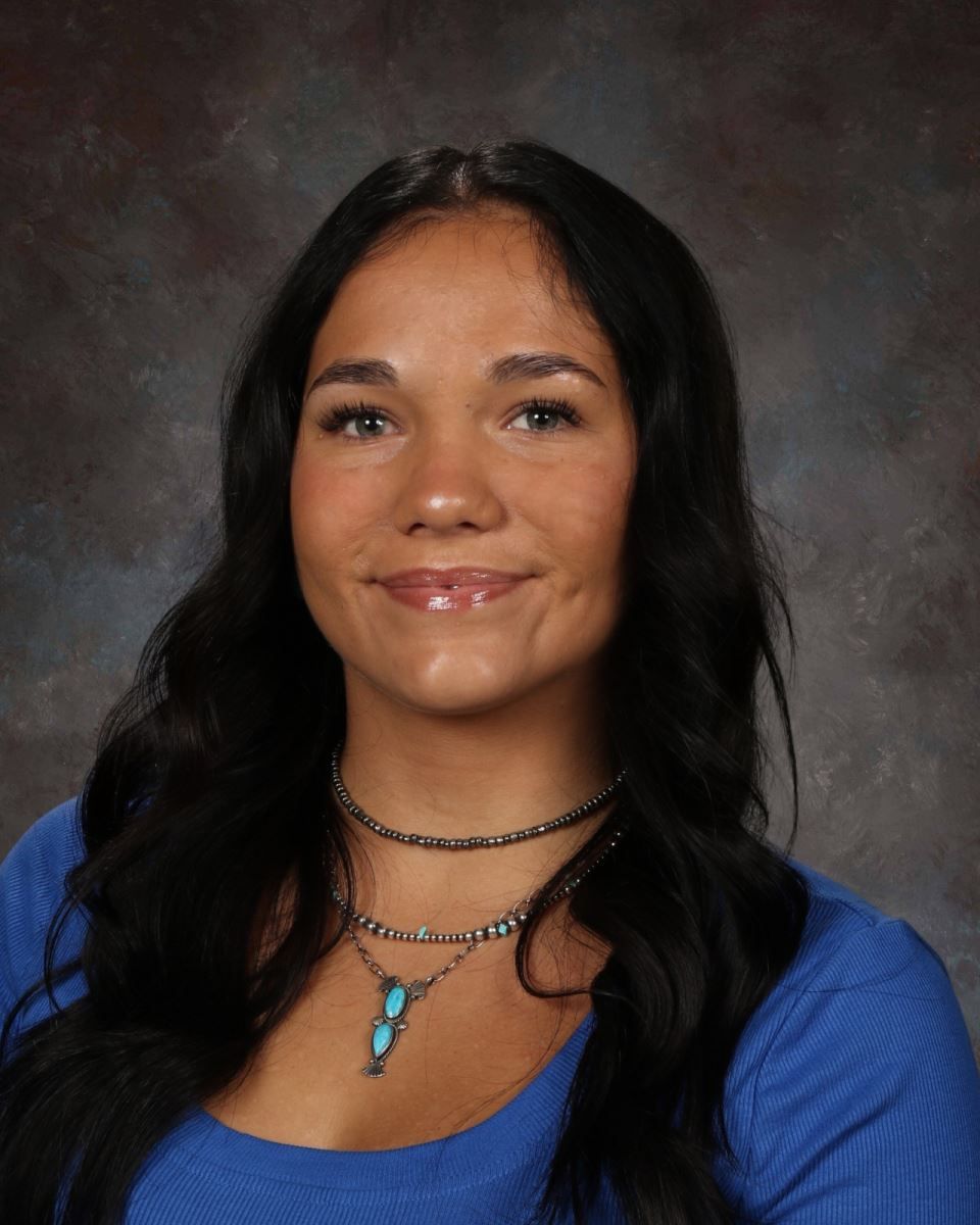 A woman wearing a choker necklace and a blue shirt is smiling for the camera.