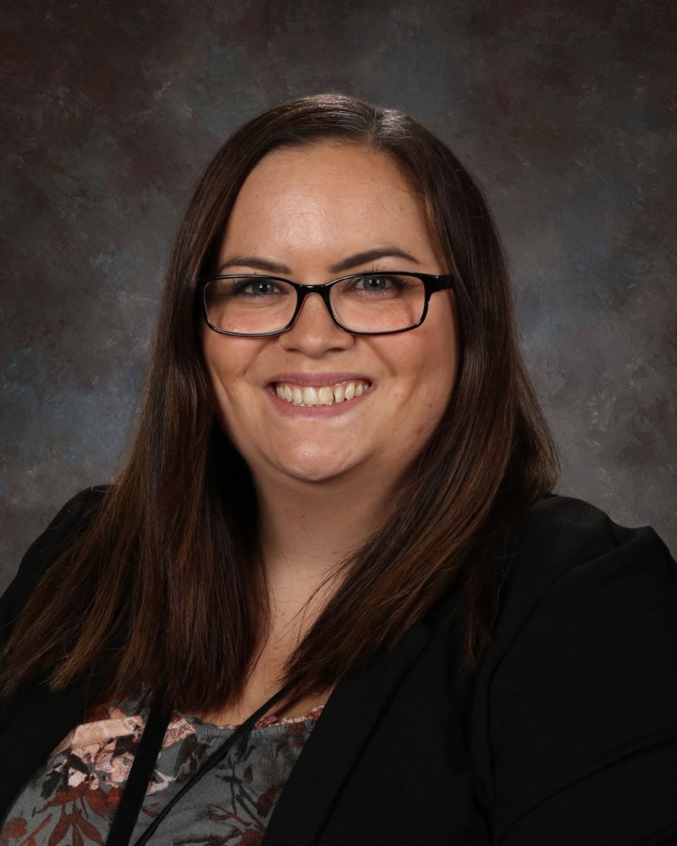 A woman wearing glasses and a black jacket is smiling for the camera.