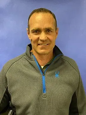 A man wearing a gray sweater with a blue zipper is smiling for the camera.