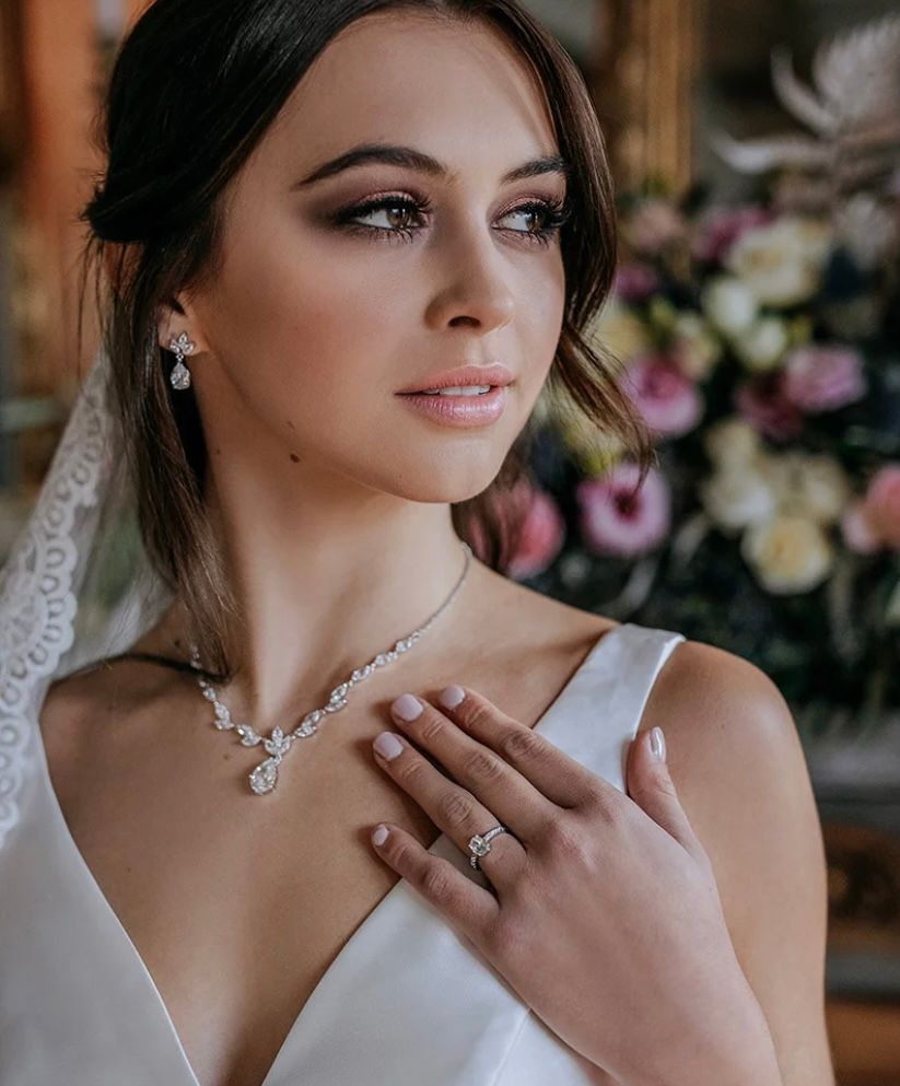 A woman in a wedding dress is wearing a necklace and a ring.