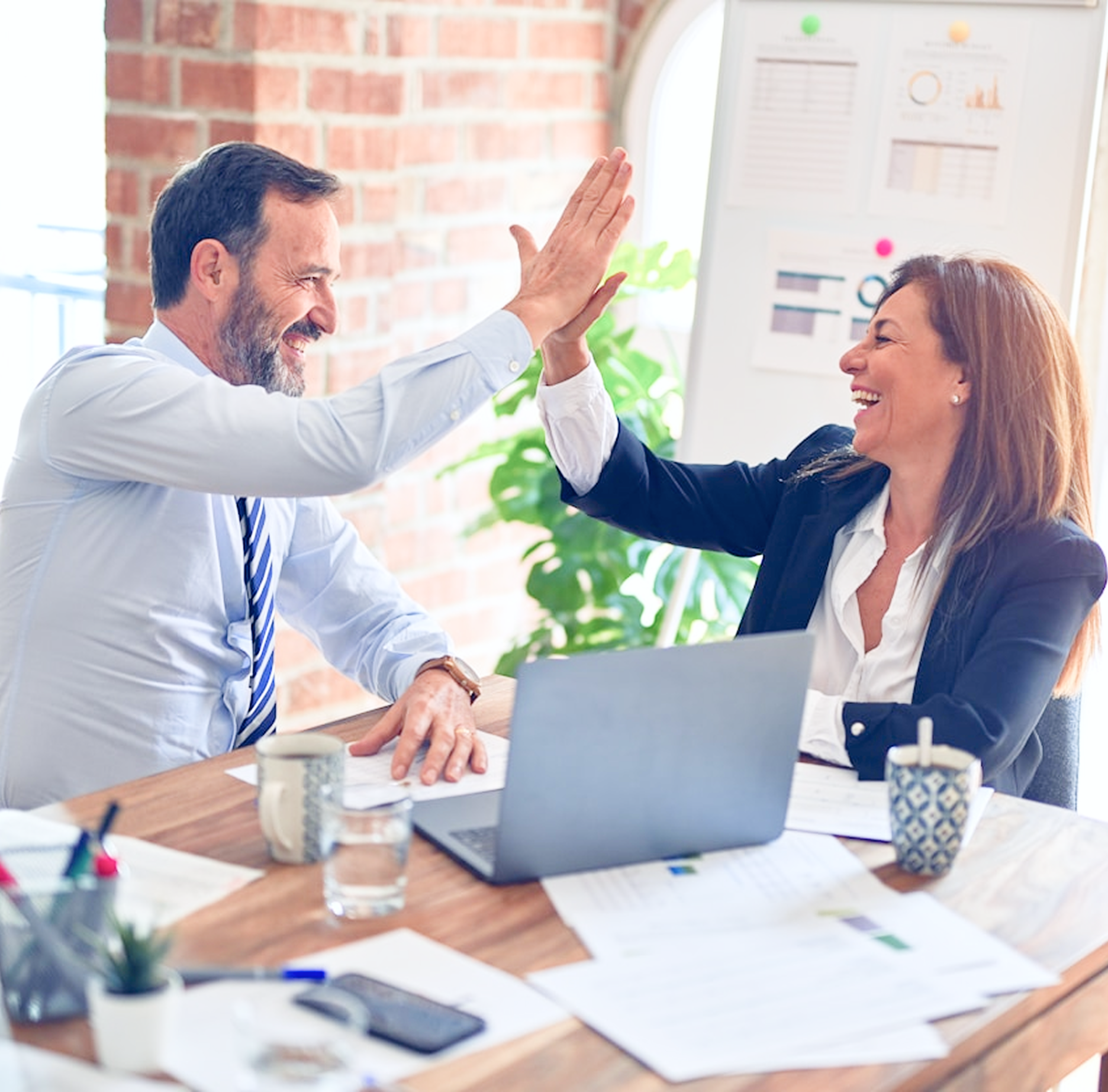 Man and woman at a desk give each other a high five, smiling.