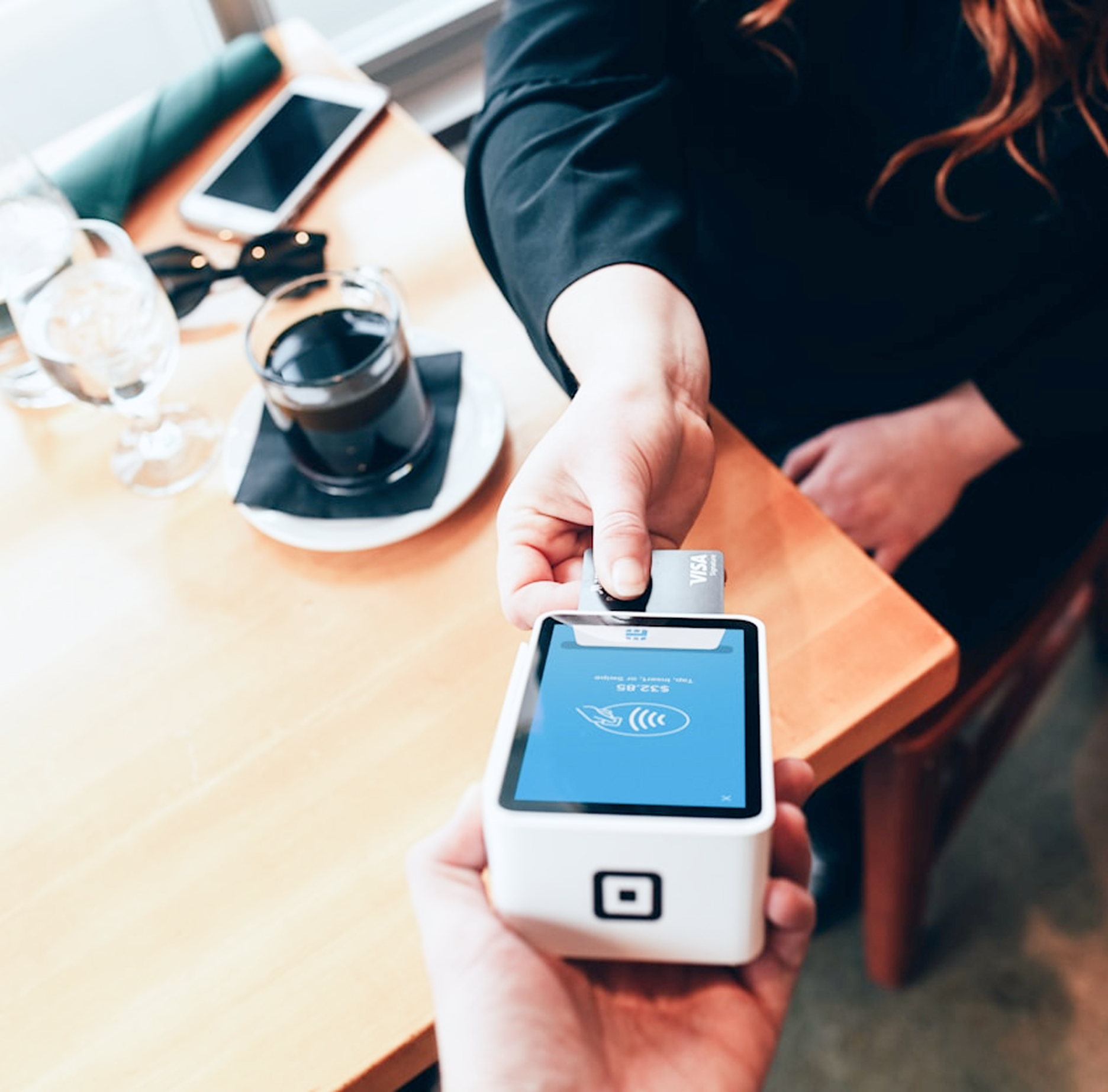 Person paying with card at a restaurant, placing card on a card reader.