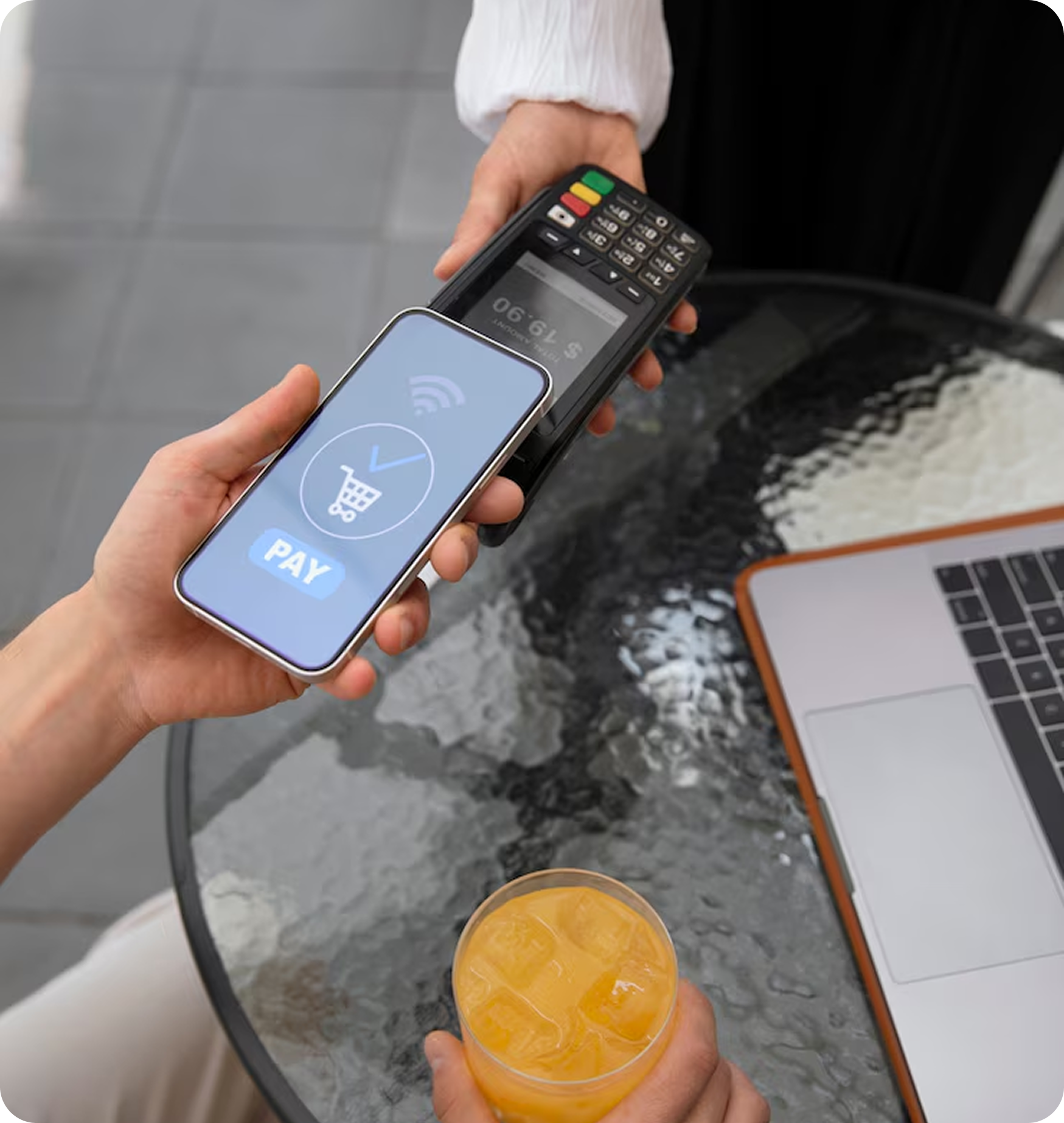 Person paying with phone at a cafe using contactless payment; juice and laptop on table.
