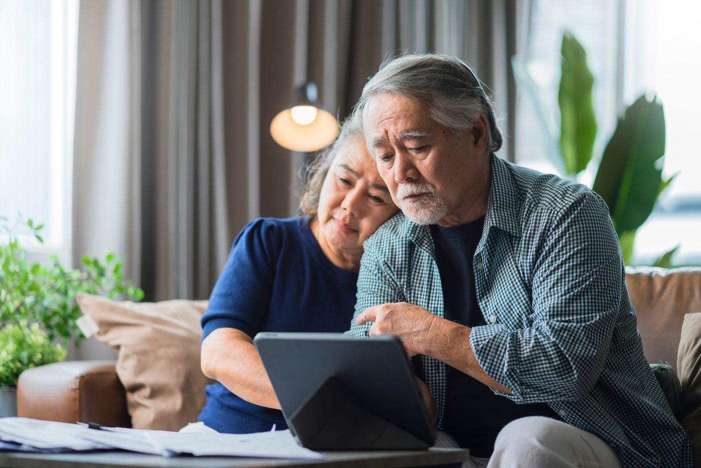 Two people studying a tablet together on a couch in a bright living room