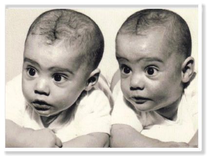 Two babies are sitting next to each other in a black and white photo.