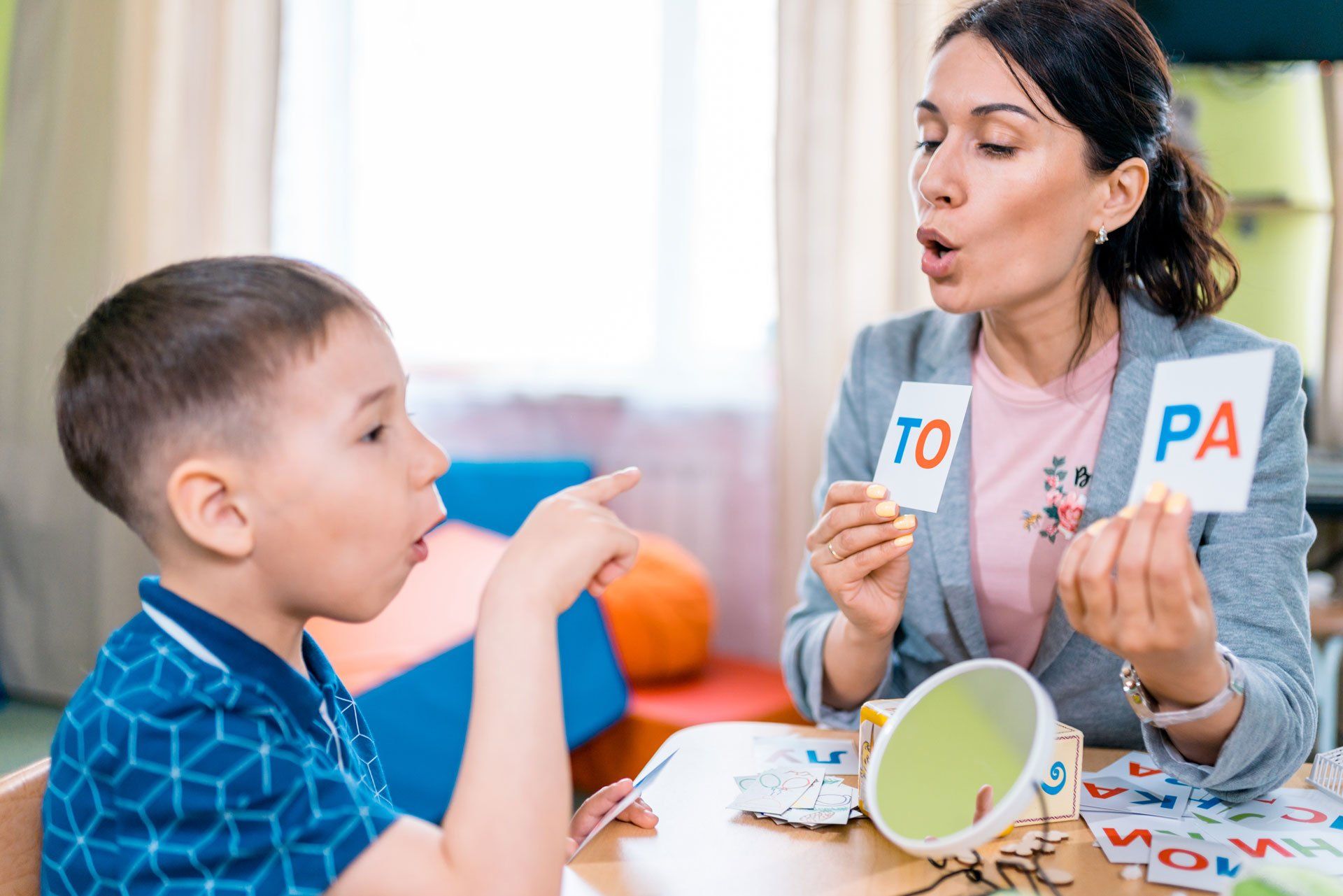 The attractive woman teacher teaches the preschool aged boy to read. The woman is holding the cards with the letters and the boy is trying to read them