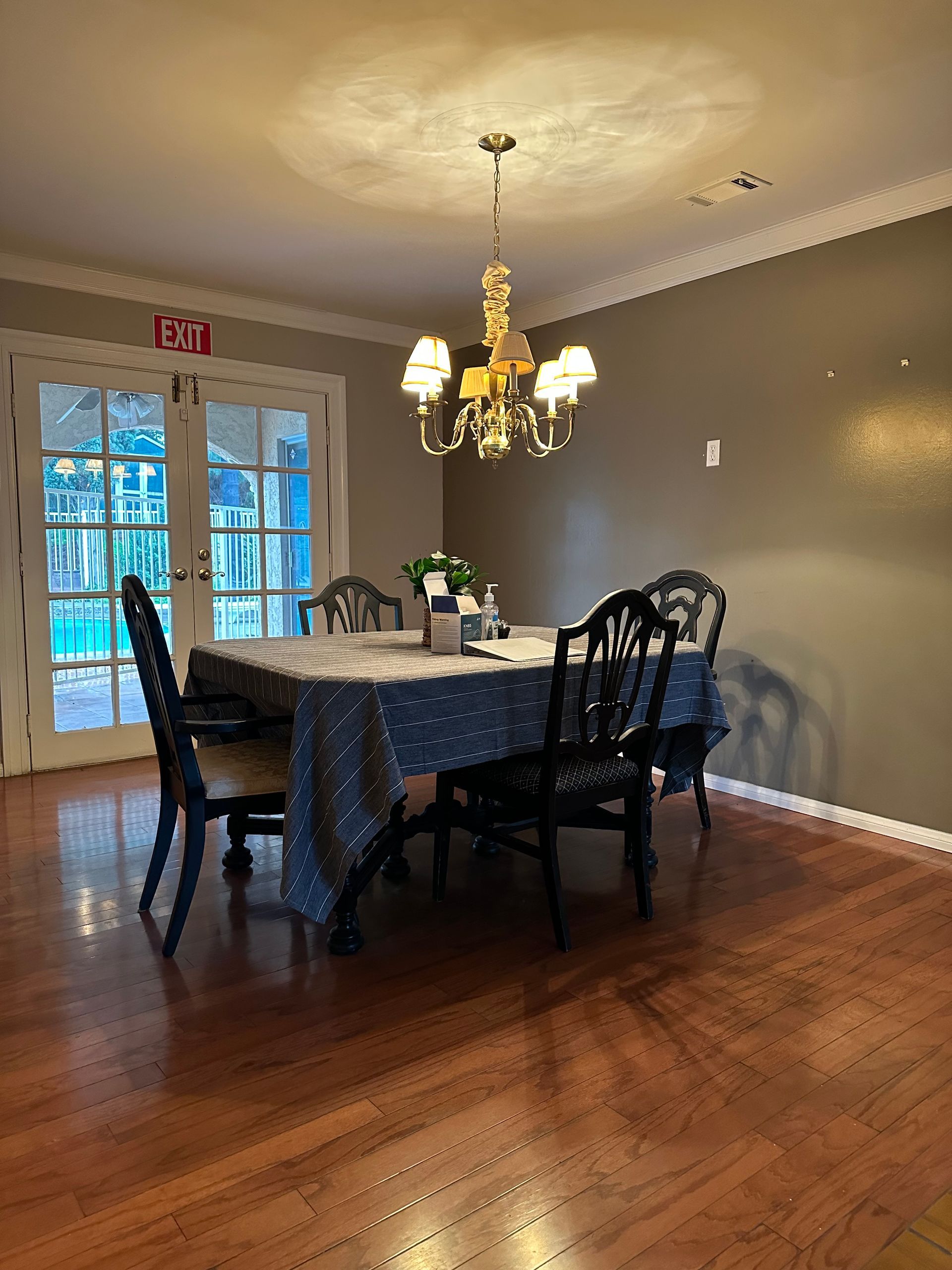 Dining room with table set for a meal. Dark wood floor, ornate chandelier, and French doors leading outside.
