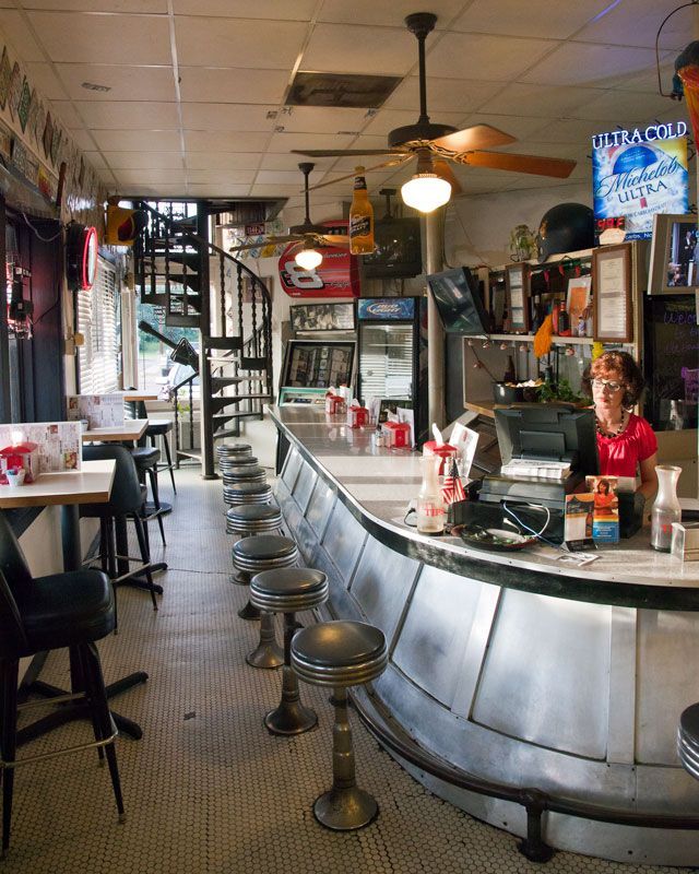 Vintage diner interior with curved counter, stools, and a seated cashier behind the register