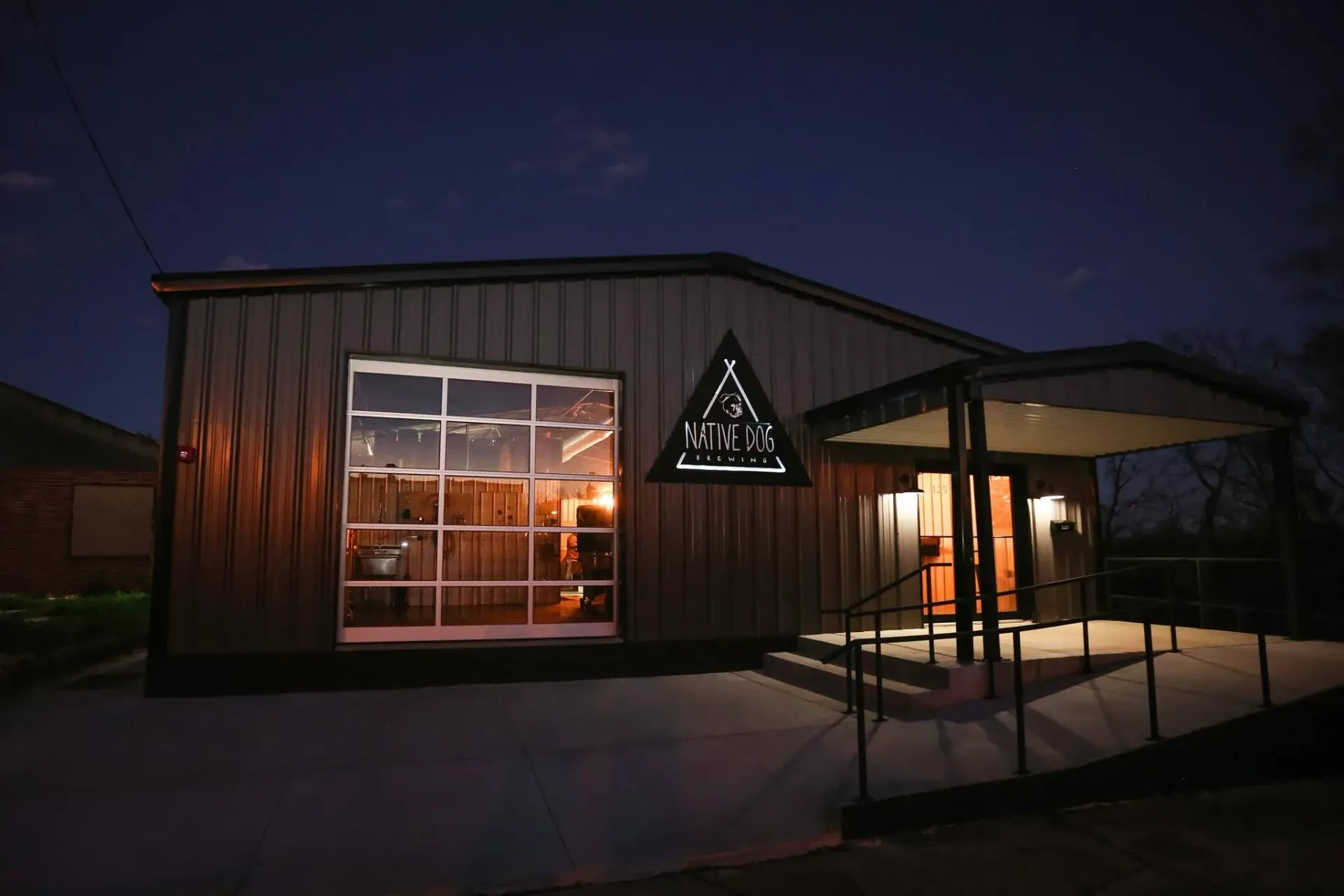 Nighttime exterior of a small building with lit windows and a triangular sign above the entrance.