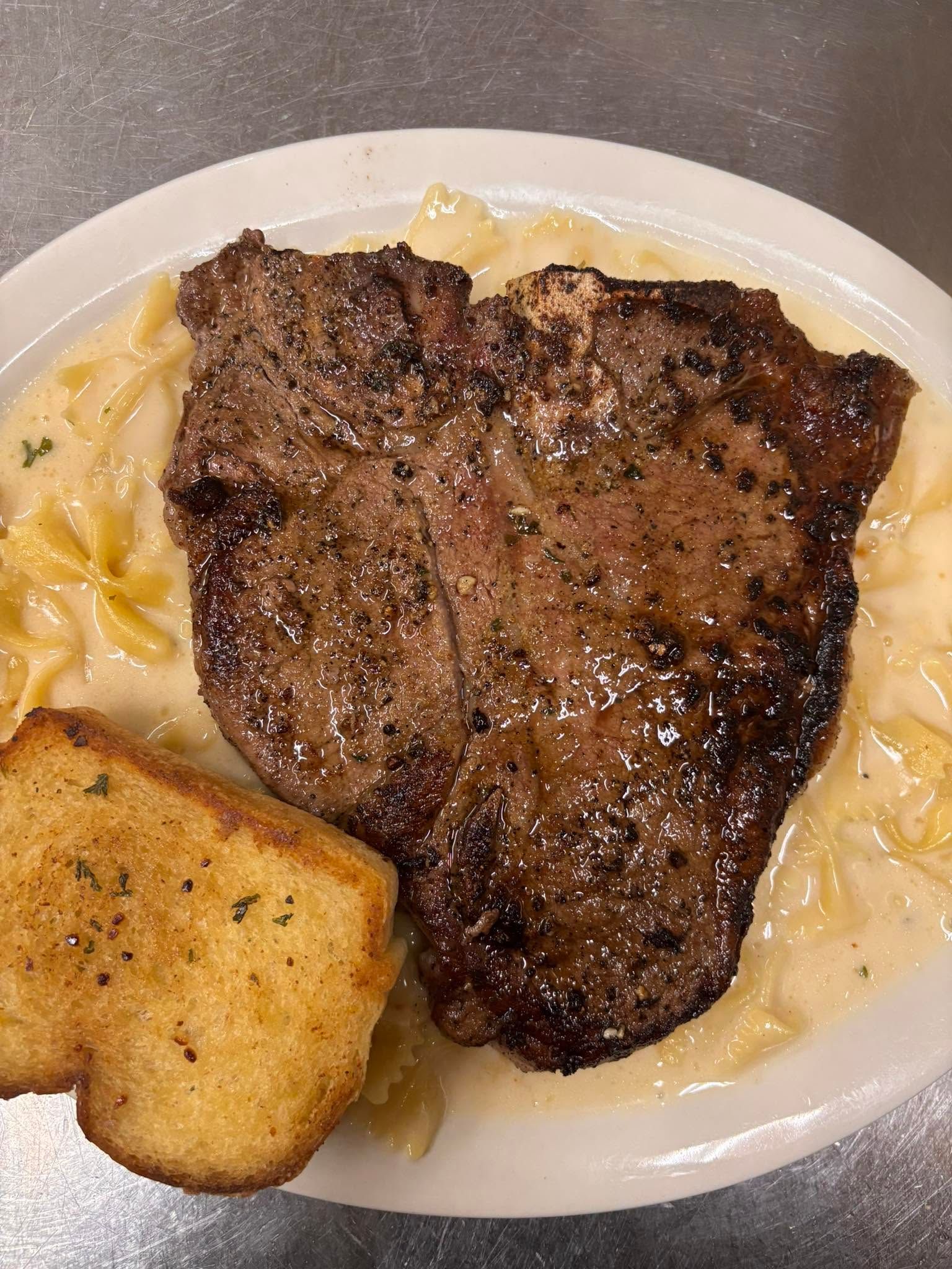 Steak on a plate with creamy pasta and a piece of garlic bread