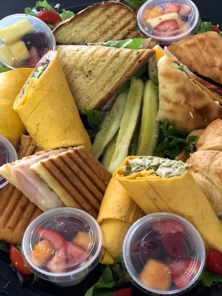 Assorted sandwiches, wraps, veggie sticks, and fruit cups arranged on a platter.