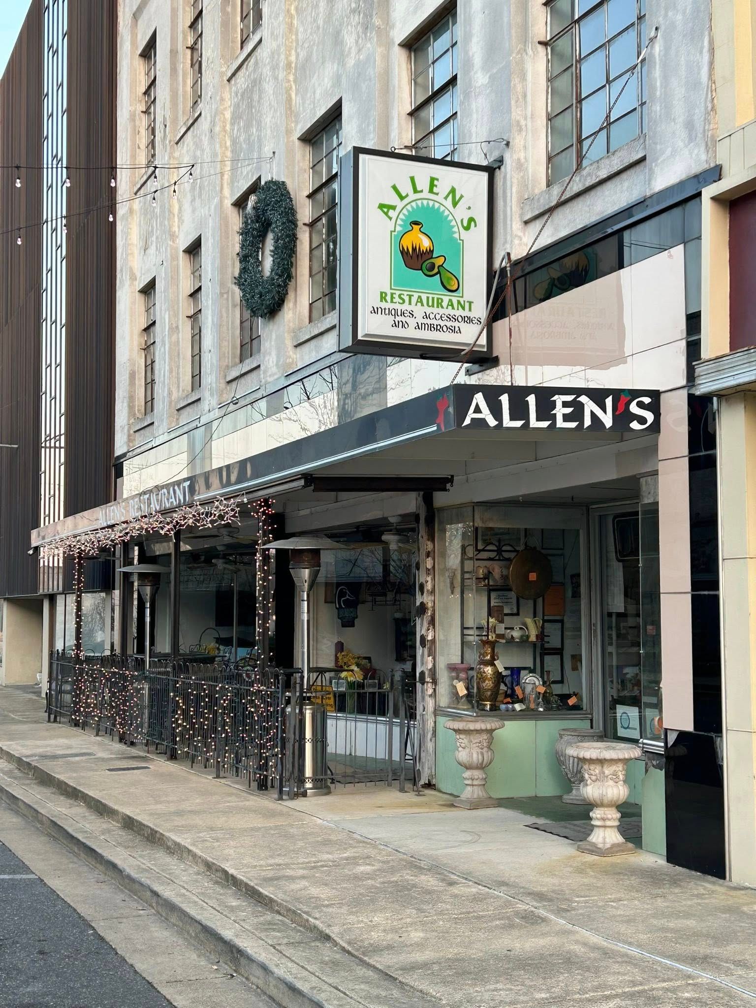 Storefront of Allen’s with a black awning, hanging sign, and street-facing display on a cobblestone sidewalk.