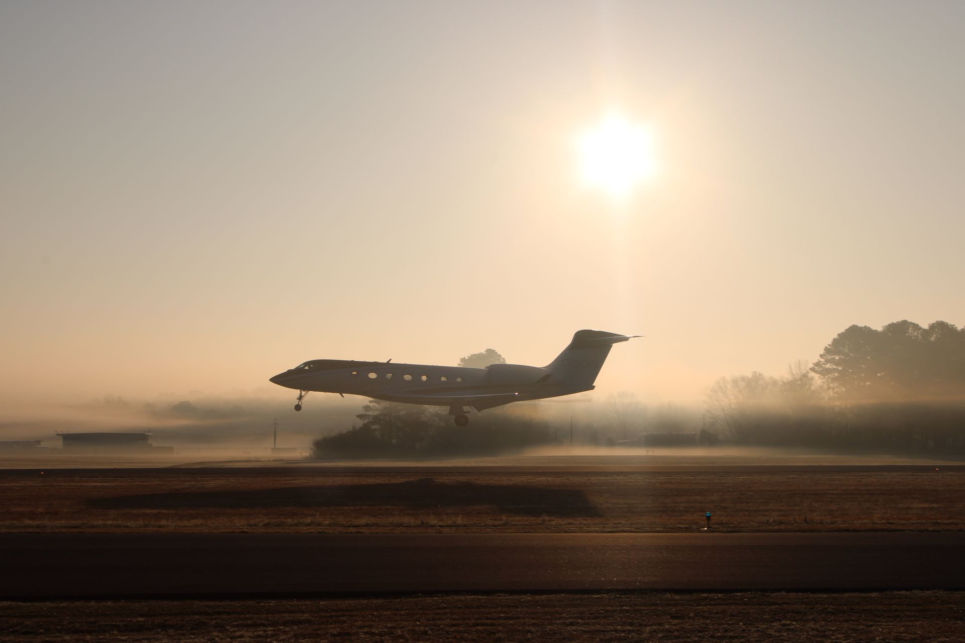 A fuel truck and a small utility vehicle parked near a private jet on an airport tarmac under a clear blue sky.
