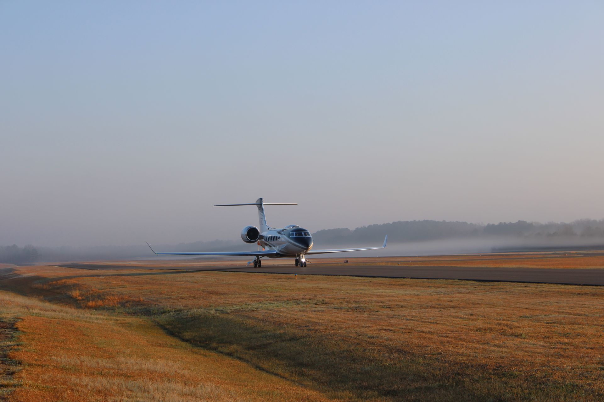 A white private jet with red accents parked on an airport tarmac near buildings at dawn.