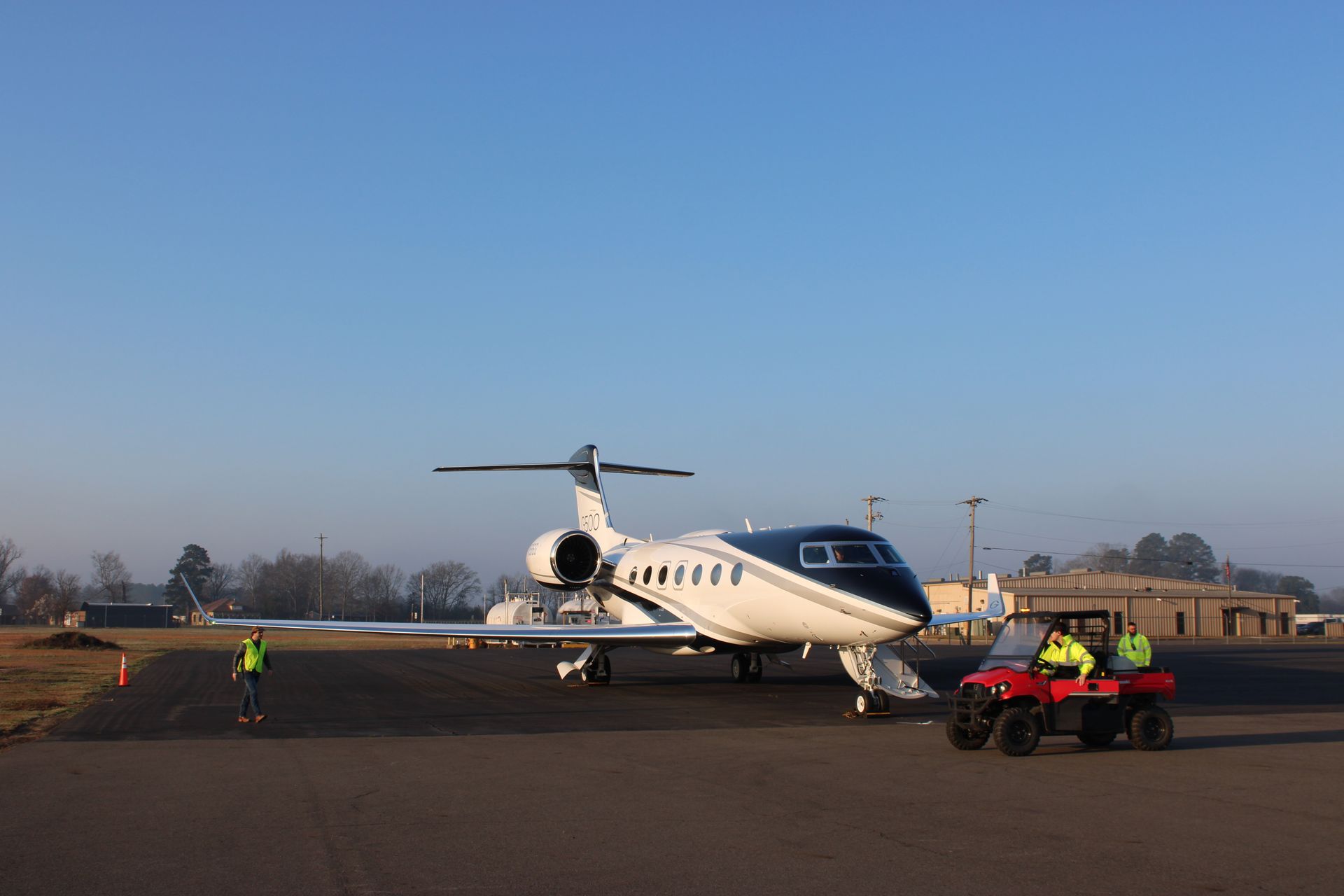 Two people wearing neon safety vests fuel a private jet on an airport tarmac.