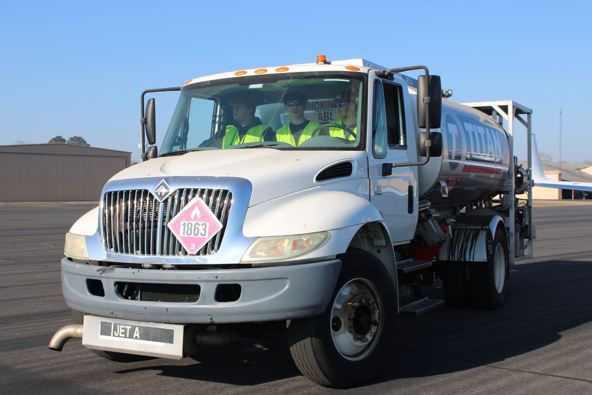 Silver tanker truck driving on a road under a clear sky