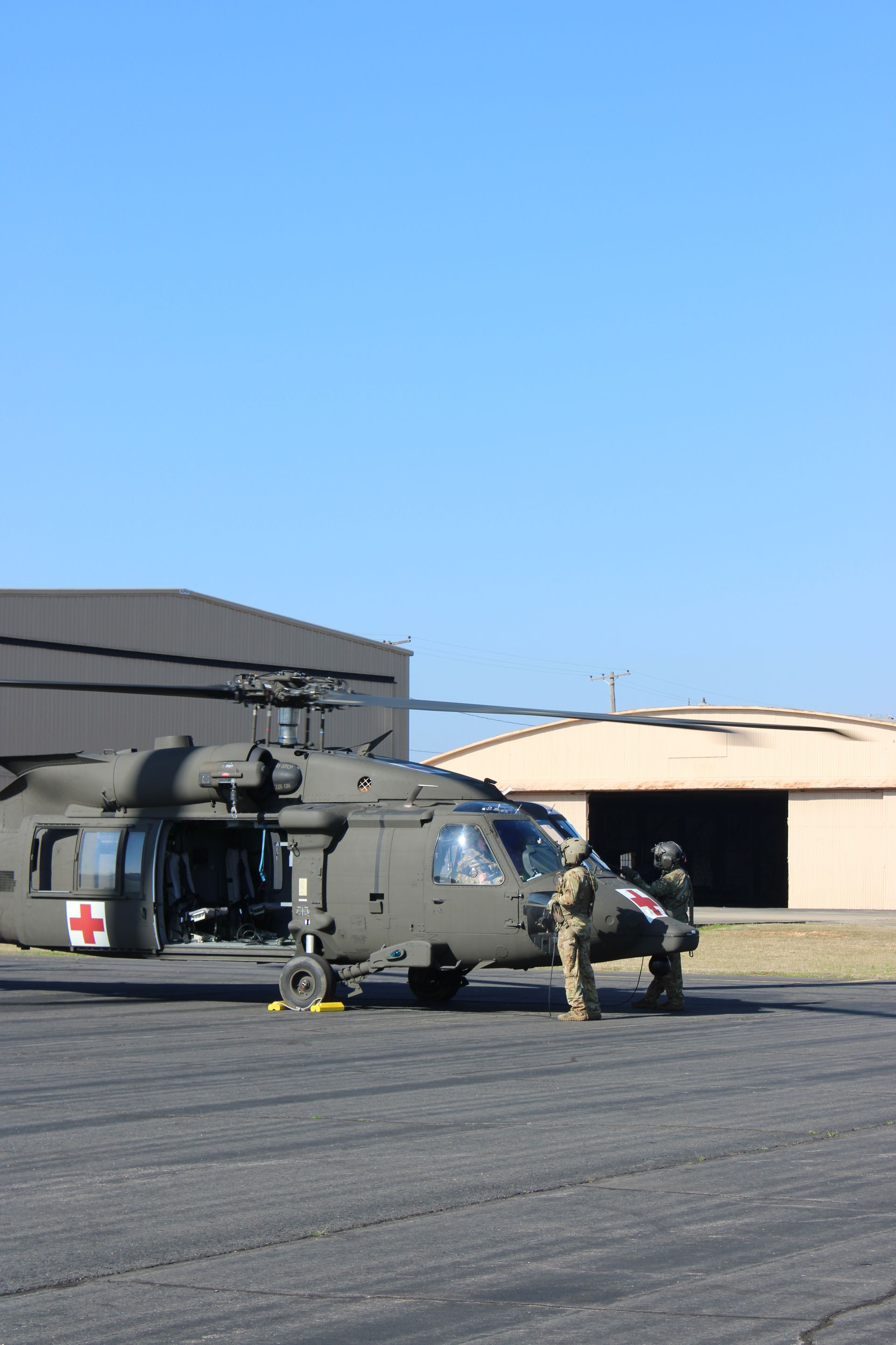 Two personnel in military uniform stand near a parked medical evacuation helicopter on an airfield.