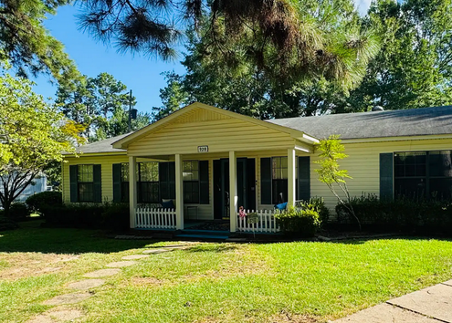 Single-story house with yellow siding, front porch, and green lawn on a sunny day