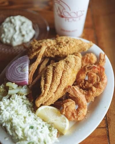 Plate of fried seafood with rice, onion, lemon, and dipping sauce on a wooden table