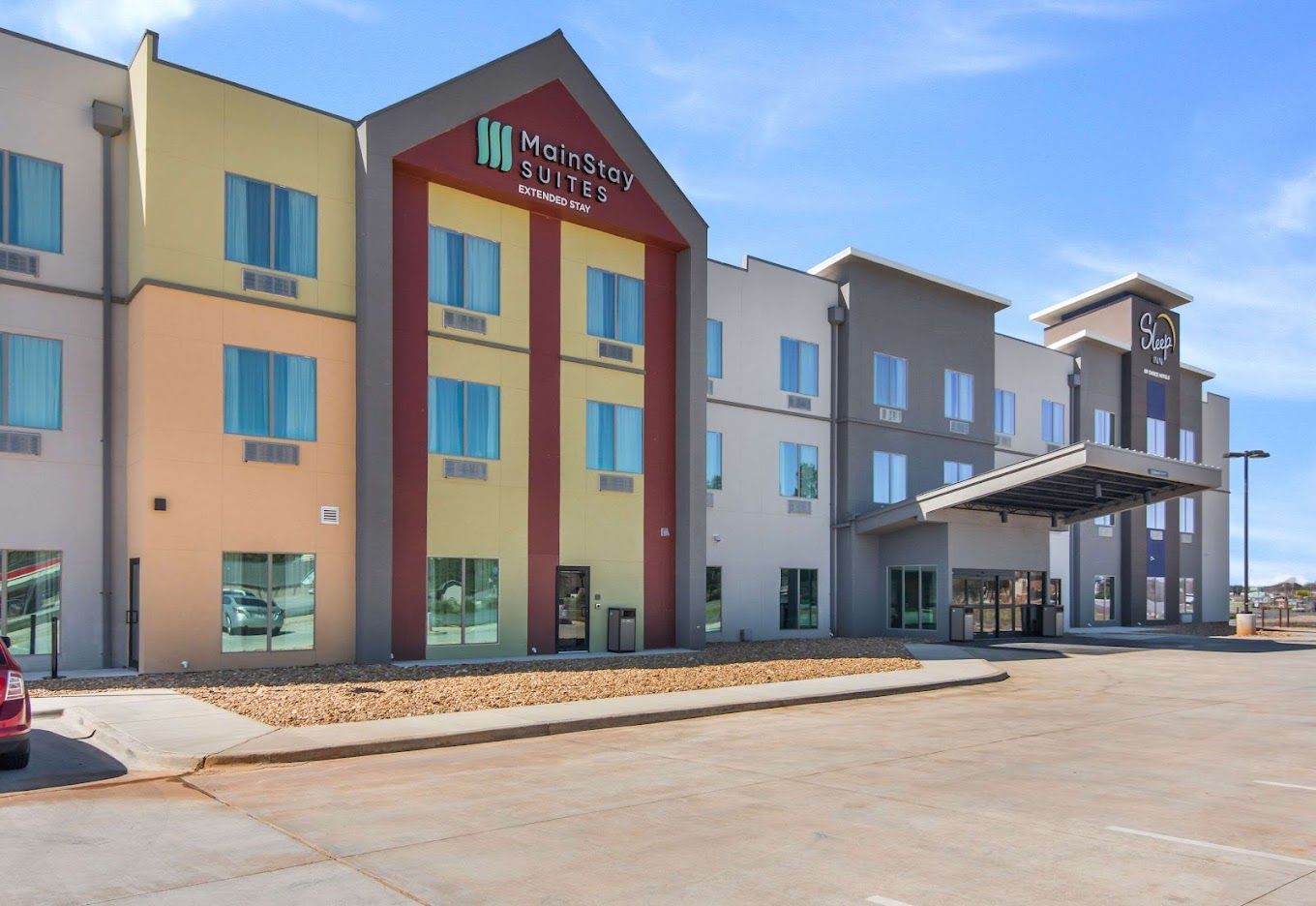 Modern hotel exterior with beige and blue walls, red accent entrance, and covered drop-off area