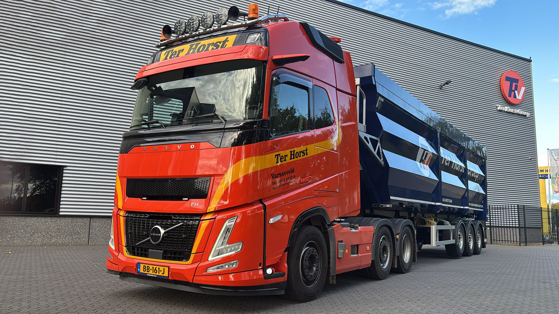 Yellow loader scoops scrap metal in a junkyard under a cloudy sky.