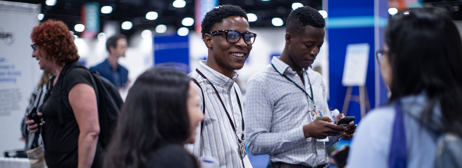 People networking at a conference booth, with one man smiling and holding a device.