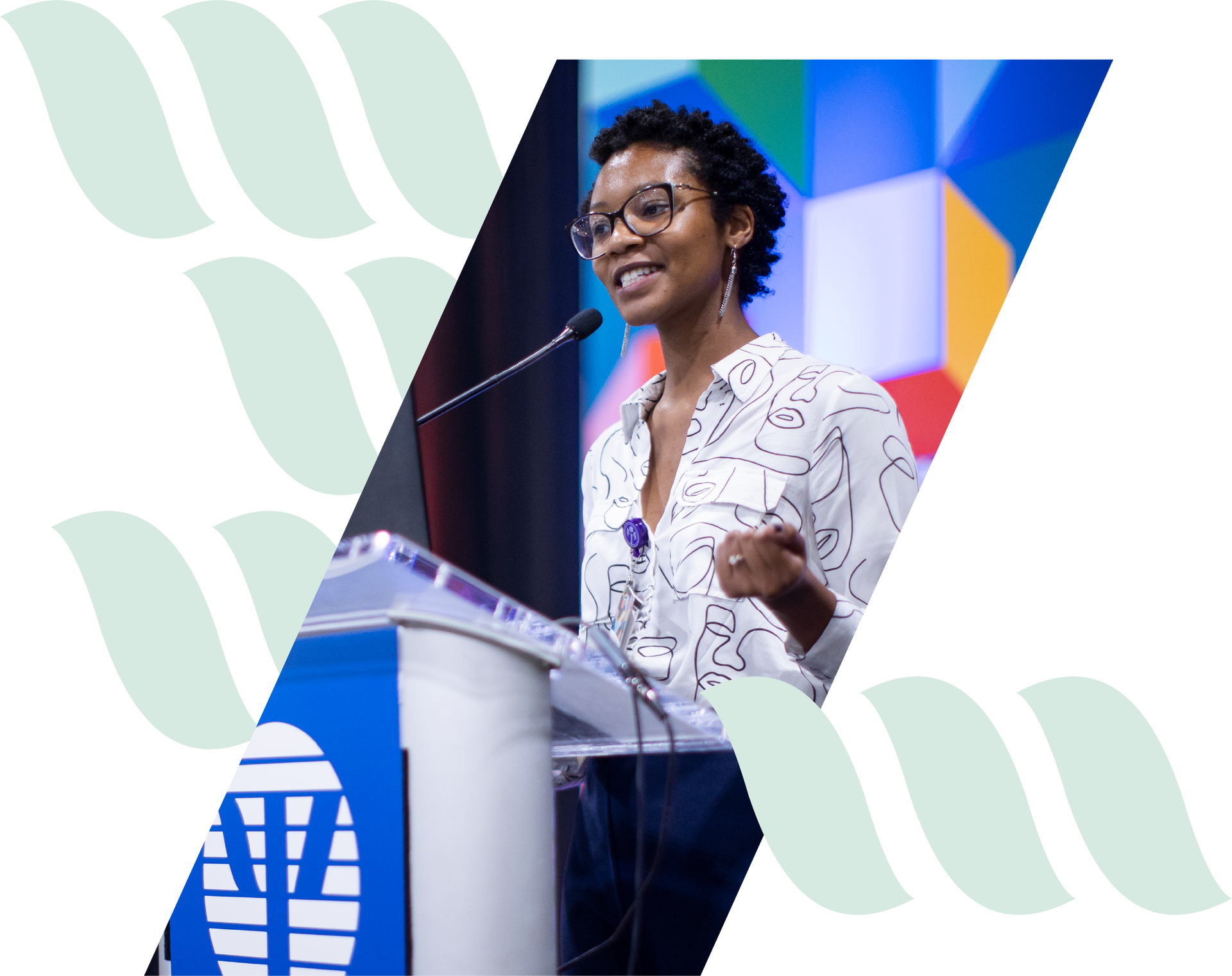 Speaker at podium giving a presentation on a colorful stage, gesturing while speaking into a microphone.