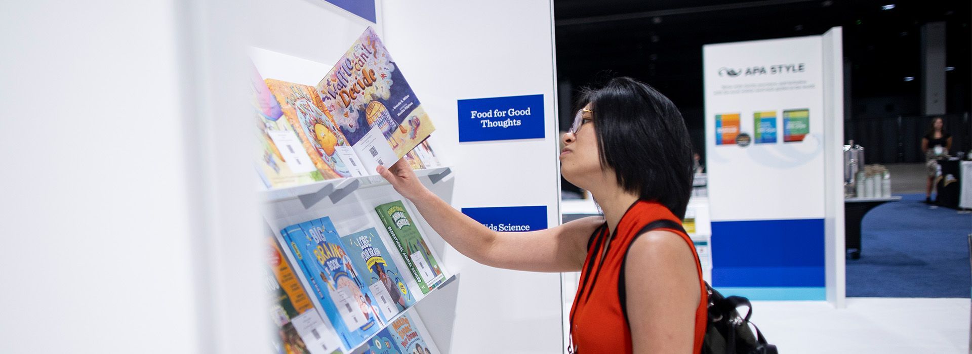 Woman in red top browsing a display of books at a trade show booth.