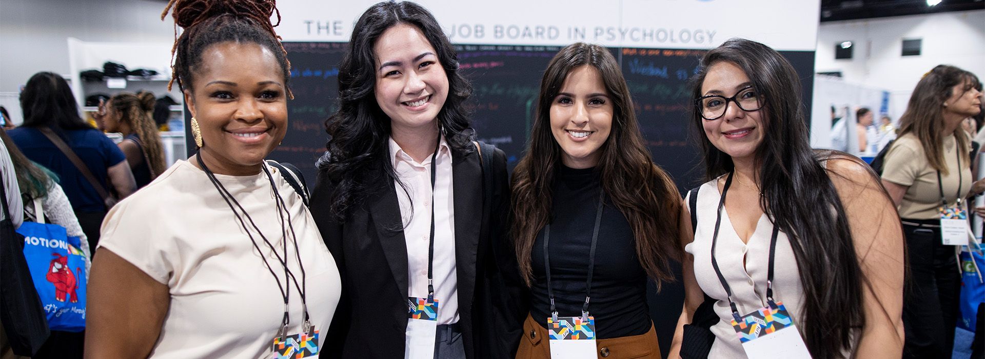 Four people smiling at a conference booth, standing side by side with badges and lanyards.