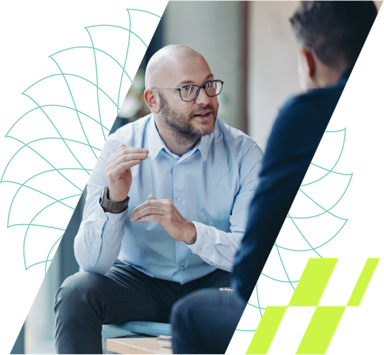 Two people in a bright office discuss at a table, with abstract teal and lime graphic accents.