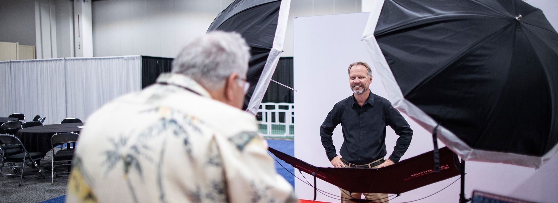 Photographer using a camera in front of a man posing beside a large black-and-white studio backdrop