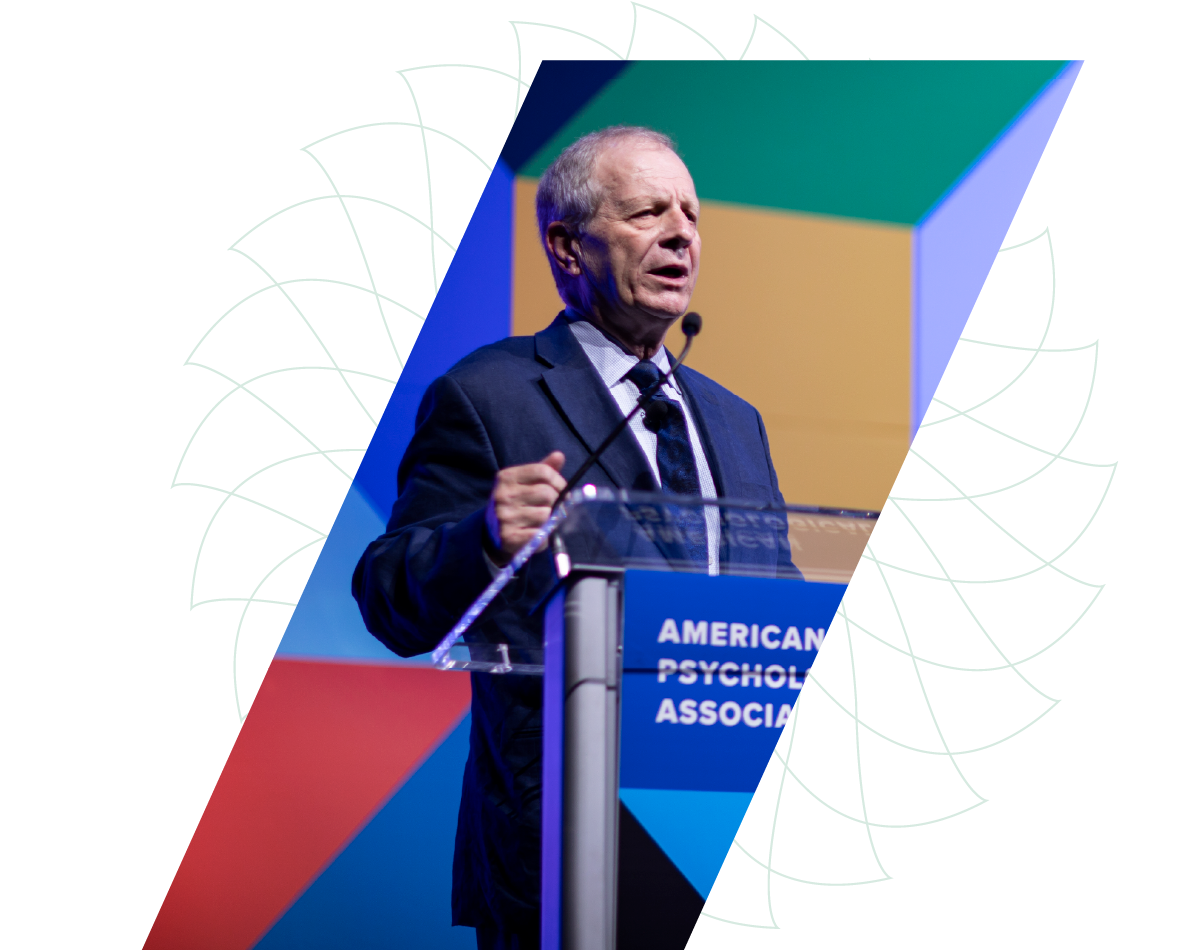 Man speaking at a podium with American Psychological Association sign against a colorful geometric backdrop