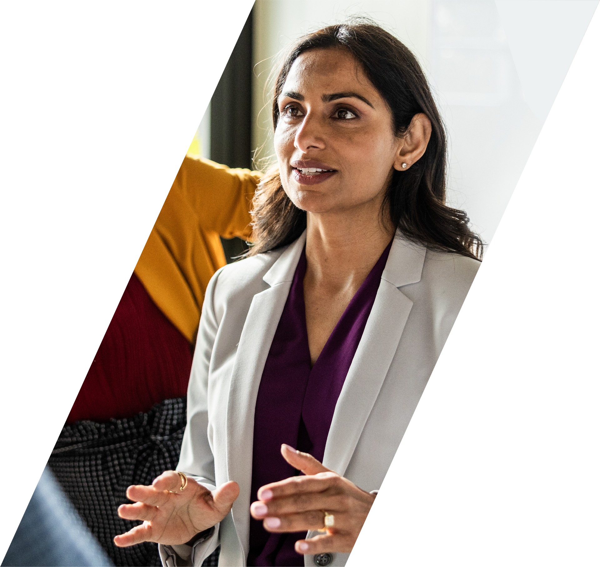 Woman in a white blazer speaking with hands raised in a bright office setting