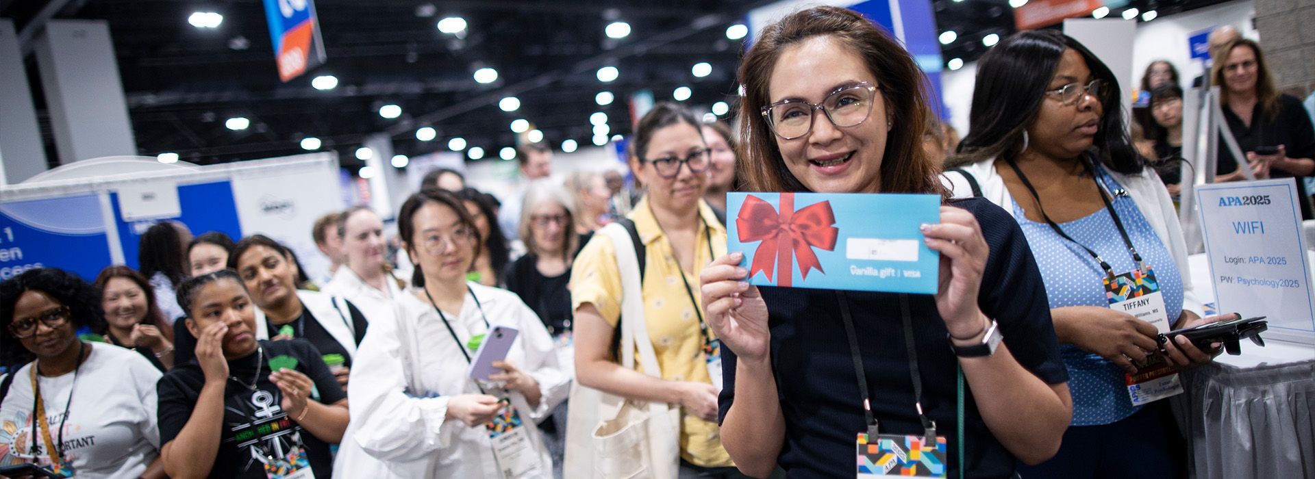 Crowd at a convention booth, with one woman smiling and holding up a blue card in front of a colorful display.