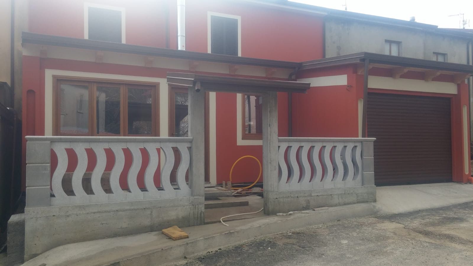 Una casa rossa con balcone e garage in costruzione.