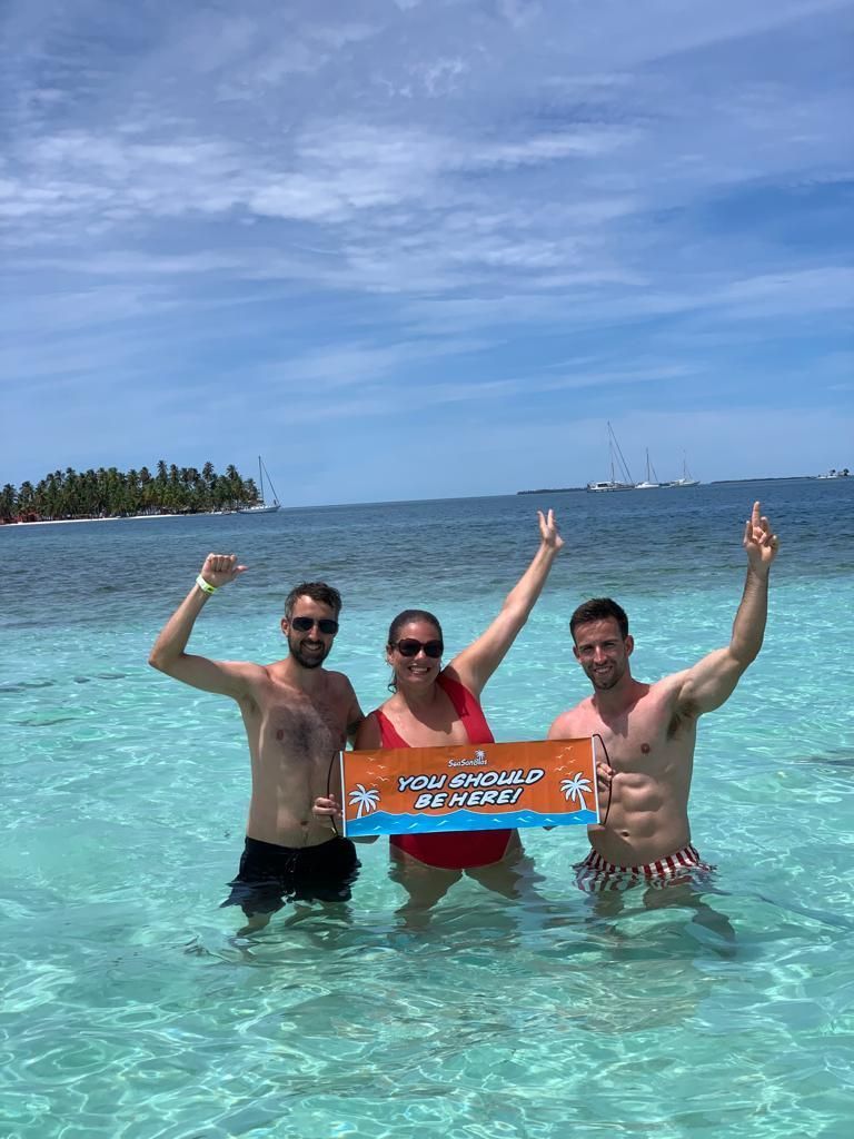Three people are standing in the water holding a sign.