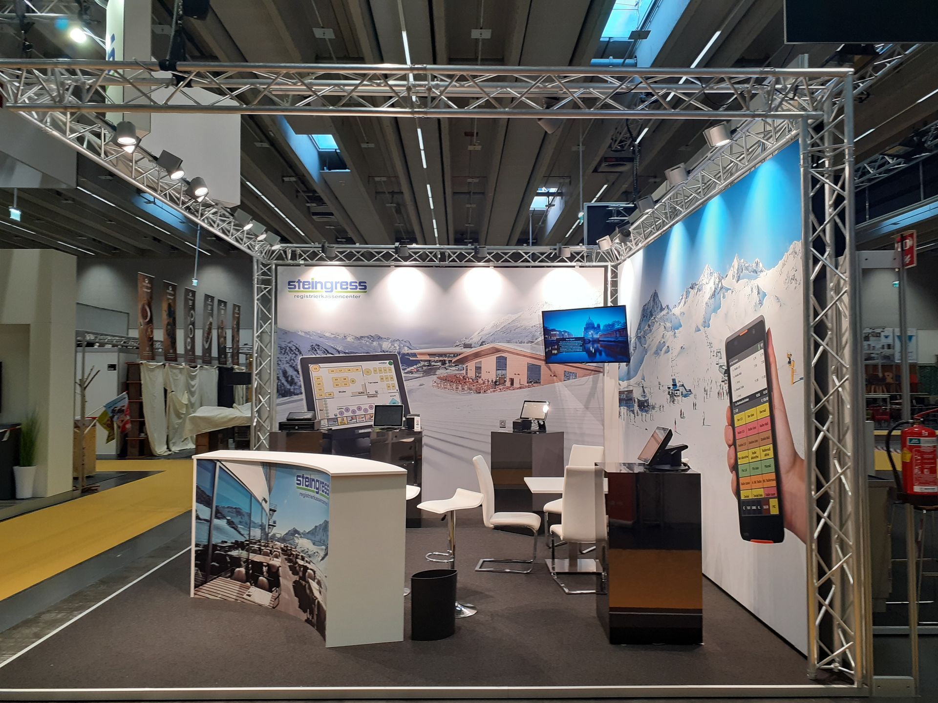 Ein Stand mit Tischen und Stühlen und einem großen Bildschirm an der Wand