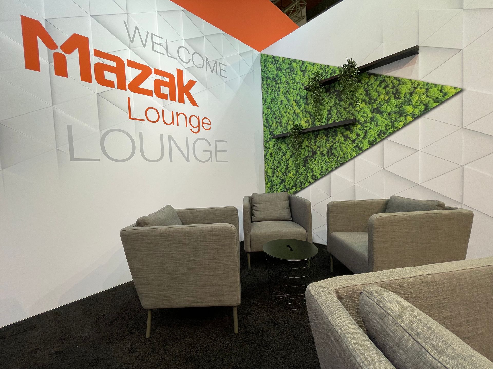 Ein Raum mit Stühlen und einem Tisch vor einer Wand mit der Aufschrift „Mazak Lounge Lounge“